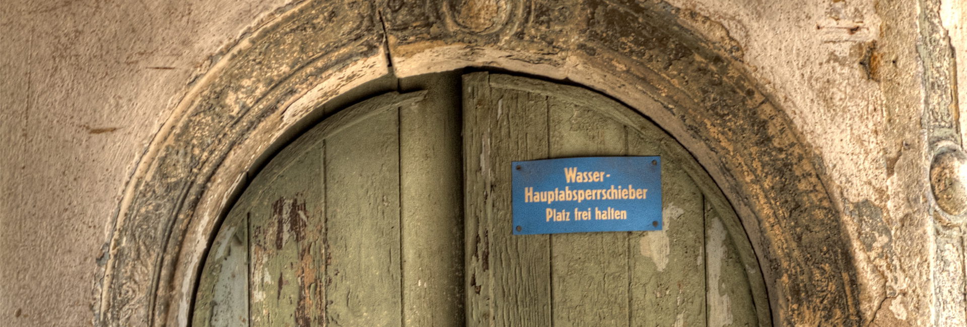 Sehr alte Holztür mit Stein und Schild.